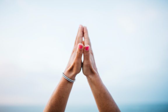 Manos juntas en un gesto de agradecimiento o meditación contra un cielo claro.