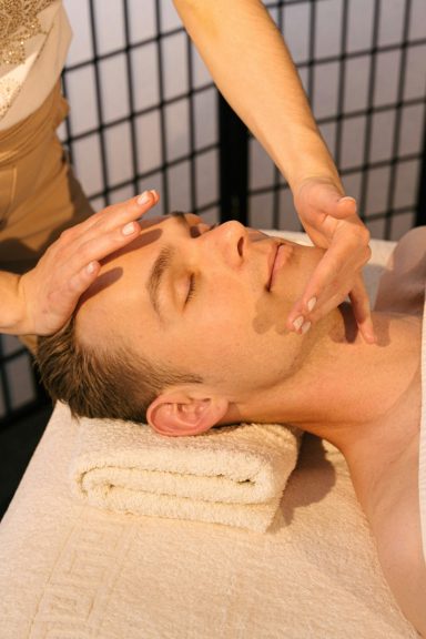 Hombre recibiendo un masaje facial, con una mano en su frente y una toalla debajo.